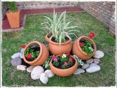 four clay pots with plants in them on the grass next to some rocks and flowers