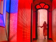 a woman standing in an open door to a room with red and blue lights on the walls