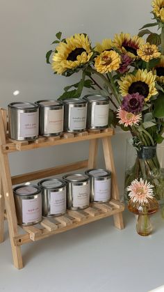 a vase filled with yellow and purple flowers sitting next to a wooden shelf holding candles