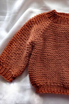 an orange knitted sweater laying on top of a white bed sheet with the bottom half turned down