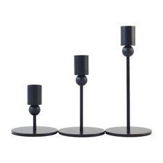 three black candles are lined up next to each other on the same stand, with one candle in between them