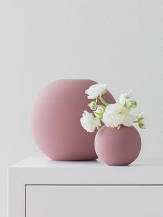 two pink vases with white flowers in them on a table next to a wall