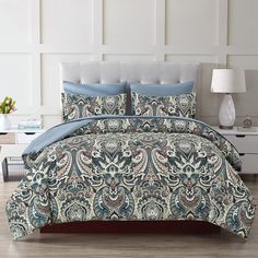 a bed covered in a blue and white comforter next to a night stand with a lamp