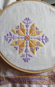 an embroidered cross on a white piece of cloth with purple and gold trimmings