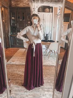 a woman taking a selfie in front of a mirror wearing a long maroon skirt