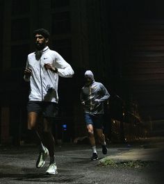 two men running in the street at night with one wearing a white jacket and black shorts