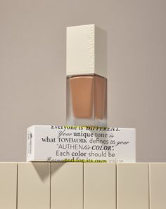 a bottle of makeup sitting on top of a white tile wall next to a box