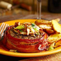 a yellow plate topped with meat covered in toppings next to fries and a glass of wine