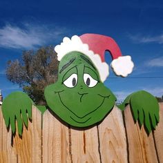 a wooden fence with a green grin face on it's side and a santa hat on its head