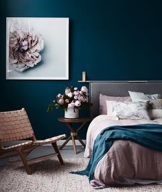 a bedroom with blue walls and pink flowers on the bed, next to a chair