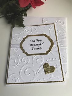 a white card with gold glitter hearts on it and a red rose in the background