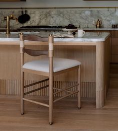 a kitchen with wooden cabinets and marble counter tops, along with a bar stool that has a white upholstered seat