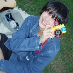 a woman sitting on the grass with a camera in her hand and smiling at the camera