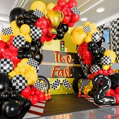 the balloon arch is decorated with black, yellow and red balloons that read two fast