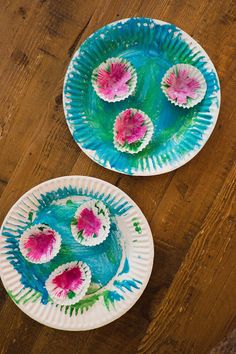 two paper plates with flowers painted on them sitting on a wooden table next to each other