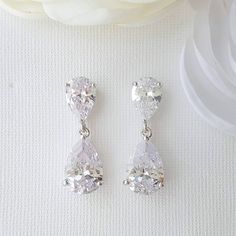 two pairs of white cubicge earrings on top of a white cloth with flowers in the background