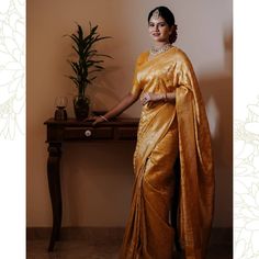 a woman in a gold sari standing next to a table with a potted plant