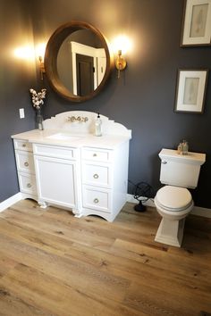 a white toilet sitting next to a sink in a bathroom under a large round mirror