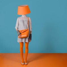 a woman with orange tights and an orange purse standing in front of a blue wall