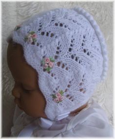 a baby doll wearing a white crochet hat with pink flowers on it's head