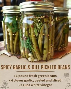 three jars filled with pickled beans on top of a wooden table next to a sign that says spicy garlic and dill pickled beans