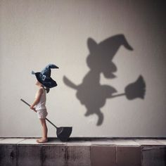 a little boy with a hat and broom casting a shadow on the side of a wall