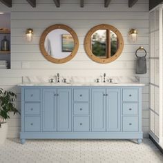 a bathroom with two round mirrors above the sinks and blue cabinetry on the wall