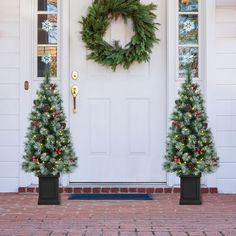 two christmas trees in front of a white door with a wreath on the top and bottom