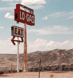 an old gas station sign in the middle of nowhere, with mountains in the background