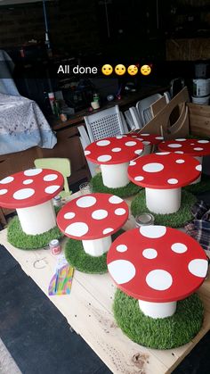 four red mushrooms sitting on top of green grass covered ground next to chairs and table