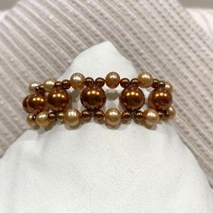 Copper and gold Swarovski crystal pearls of various sizes have been woven by hand into a luxurious bracelet fastened with a copper toggle clasp.  The bracelet is about 7 3/4 inches long.  Comes nestled on a bed of cotton in a white cardboard jewelry box.  NA-444-C25 Gold Pearl Crystal Bracelet With Round Beads, Gold Beaded Pearl Bracelet For Formal Occasions, Elegant Brown Beaded Bracelets, Luxurious Bracelet, Cardboard Jewelry, Cardboard Jewelry Boxes, Coin Bracelet, Shell Bracelet, Freshwater Pearl Necklaces