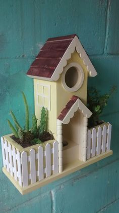 a yellow birdhouse with a brown roof on a shelf next to a white picket fence