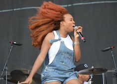 a woman with red hair singing into a microphone while standing next to two drums on stage