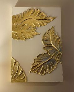 three gold leaves on white paper hanging from the wall