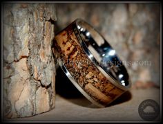 two wedding rings with wood inlays are sitting next to a tree