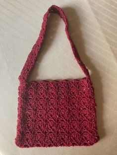 a red crocheted purse sitting on top of a white tablecloth covered bed