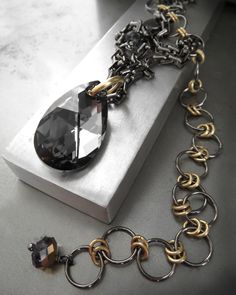 Edgy, urban, modern - a bold, sparkling teardrop crystal pendant in rich, dark 'Silver Crystal Night' charcoal is suspended from a glossy, substantial black gunmetal chain by a thick, large matte, gold-plated ring. This necklace can be worn several ways: Wear the necklace shorter to allow the ultra-long, sexy extension chain to drip down the back, or wear it longer for a modern, asymmetrical statement piece. The gunmetal lobster clasp is accented with crystal rondelles, with a half-coat gold fin Asymmetrical Necklace, Convertible Necklace, Black Night, Urban Modern, Blackest Night, Teardrop Pendant, Black Chain, Gold Pendant Necklace, Tiffany Heart