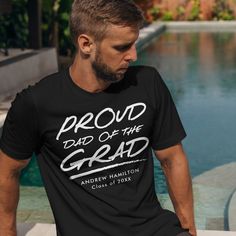 Let the special graduate in your life know how proud you are with our personalized father of the graduate t-shirt. The modern graduation t-shirt features the phrase "Proud Dad of the Grad" in white handwritten lettering with a dashed underline. Personalize the shirt by adding the graduate's name and graduation year. Cotton Graduation T-shirt, Cotton T-shirt With Text Print For Graduation, Cotton T-shirt For Graduation, Graduation Gift Short Sleeve T-shirt With Text Print, Short Sleeve Text Print T-shirt For Graduation, Graduation Gift Text Print T-shirt, Black Short Sleeve T-shirt For Graduation Gift, Pre-shrunk Short Sleeve T-shirt For Graduation Party, Short Sleeve T-shirt With Text Print For Graduation