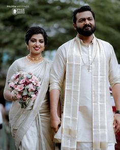 a man and woman standing next to each other in front of trees with flowers on them