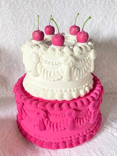 a three tiered cake with cherries on top sits on a tablecloth covered surface