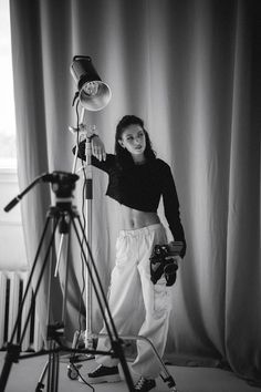 a black and white photo of a woman standing in front of a camera holding a light