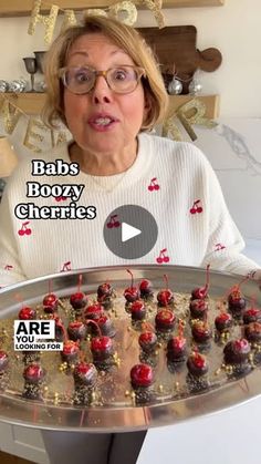 an older woman holding a tray with cupcakes and cherries on it in front of her face