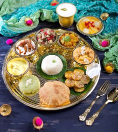 an assortment of food on a gold plate with spoons and utensils next to it