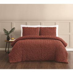 a bed with red bedspread and pillows on top of wooden floor next to wall