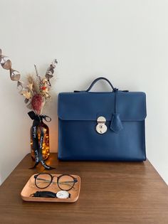 "One and only!  High quality handmade briefcase comes with navy blue colour. Everything is made by hand with great craftsmanship. This simple and minimal design will be good match with business man and woman. Outside of leather is premium italian leather that is very smooth and sleek. And inner lining is dark brown leather which has unique texture. This briefcase has one big pocket that you can put up to 13 inches laptop and two small pockets that you can put notebook or phone, passport and etc. Also I have used high quality japanese lock that gives you more tidy and simple look. Size detail : 13.7\" X 10\" X 2.8\" (35cm X 27cm X 7cm) * Merchandise on display may have some scratches on the surface. This cannot be the reason for refund or return." Luxury Blue Briefcase For Office, Formal Blue Smooth Grain Bag, Blue Luxury Briefcase For Everyday Use, Luxury Blue Briefcase For Everyday Use, Blue Top Handle Satchel For Business, Modern Blue Briefcase For Business, Modern Blue Satchel For Business, Blue Leather Briefcase For Business, Timeless Blue Business Bag