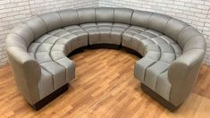 a curved couch sitting on top of a hard wood floor next to a brick wall