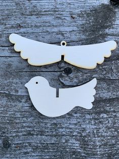 two white wooden birds with tags attached to them on a piece of wood that is laying on the ground