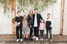 a family posing for a photo in front of a white brick wall with ivy growing on it