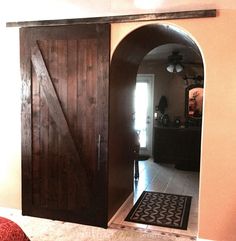 an arched wooden door is opened to reveal a bedroom with a red bed and black rug