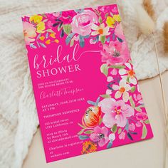 a pink and yellow floral bridal shower card on a white blanket next to some feathers